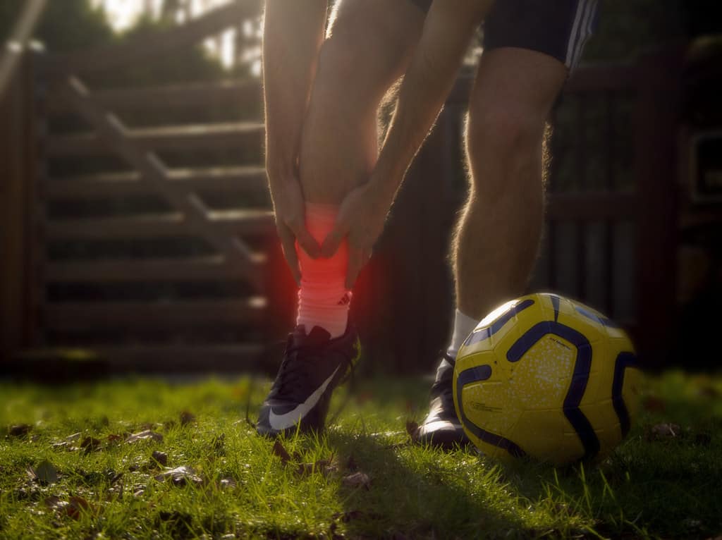 Man in football kit holding sprained ankle