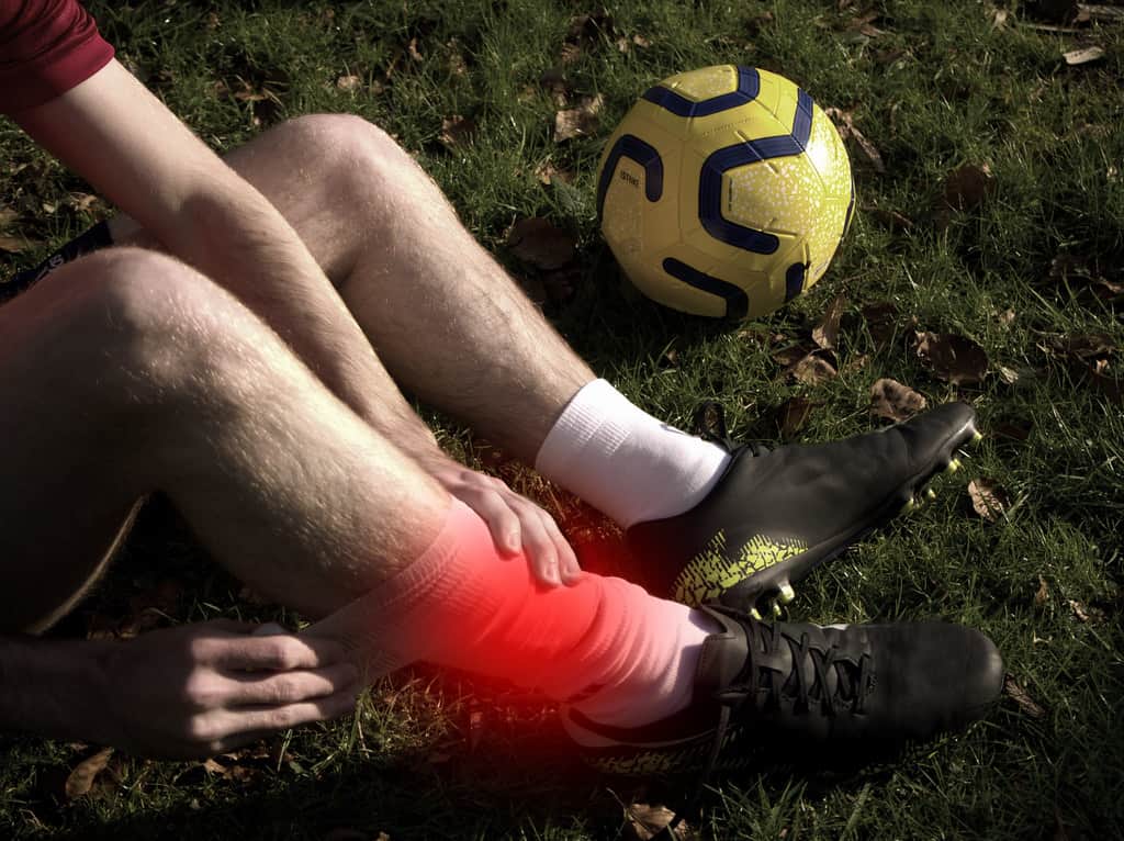 Man in football kit holding sprained ankle