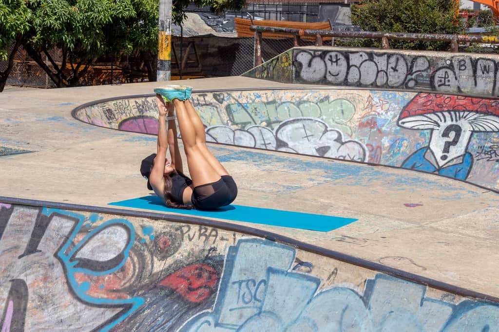 A woman doing toe touches outdoors on a yoga mat