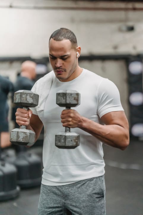 Determined ethnic sportsman exercising with dumbbells in gym