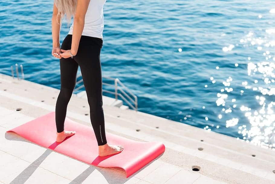 A woman stretching while standing on a yoga mat