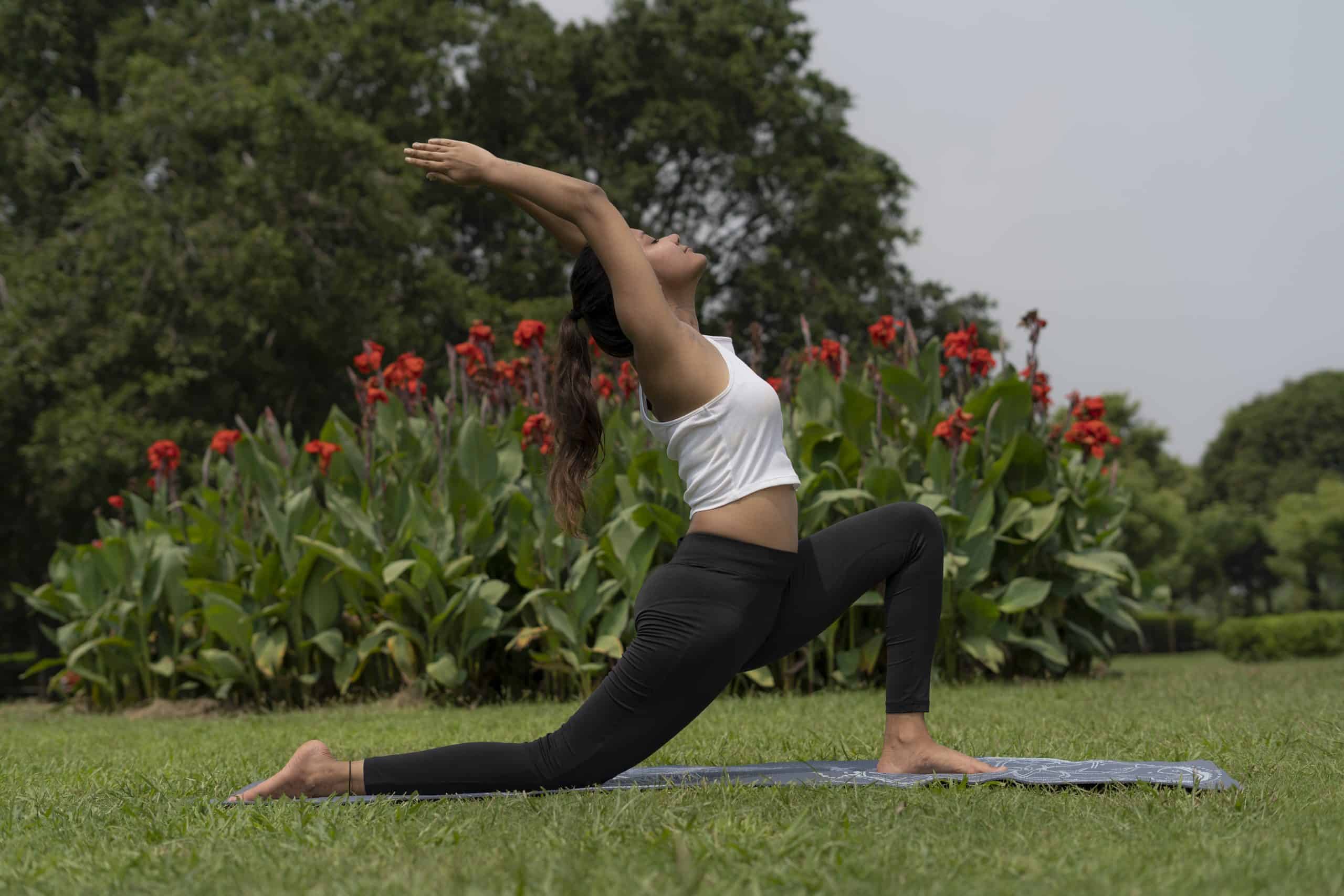 A woman doing the Warrior I pose outdoors on her yoga mat