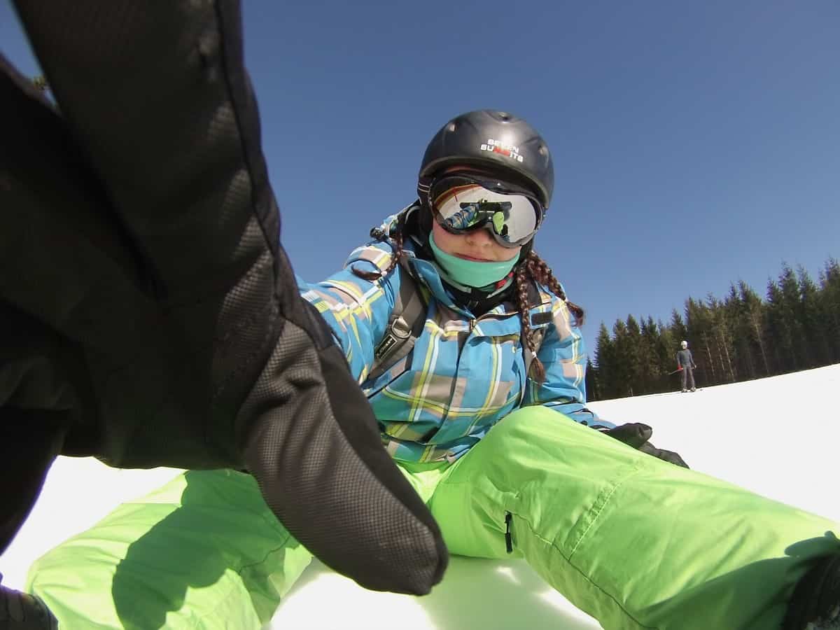 A woman snowboarding down a snowy slope, wearing full winter gear, including a helmet, goggles, jacket, and pants for winter sports injury prevention.