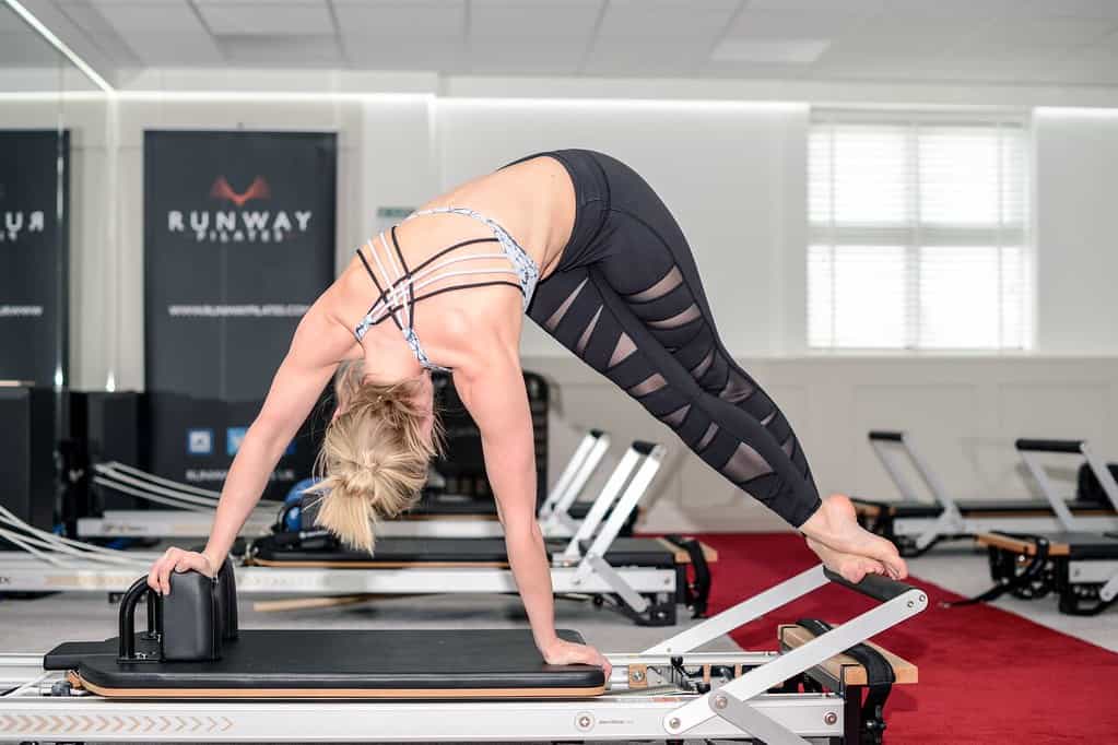 Woman practising Forward Twist Pose on Pilates reformer.