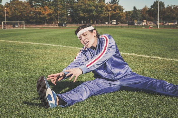 Woman athlete performing static stretching on a field.