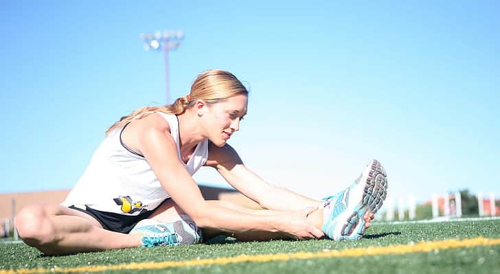 Woman runner performing static stretching on a field.
