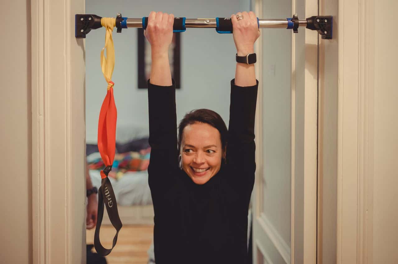 Woman using pull-up bar attached to door frame for exercise.