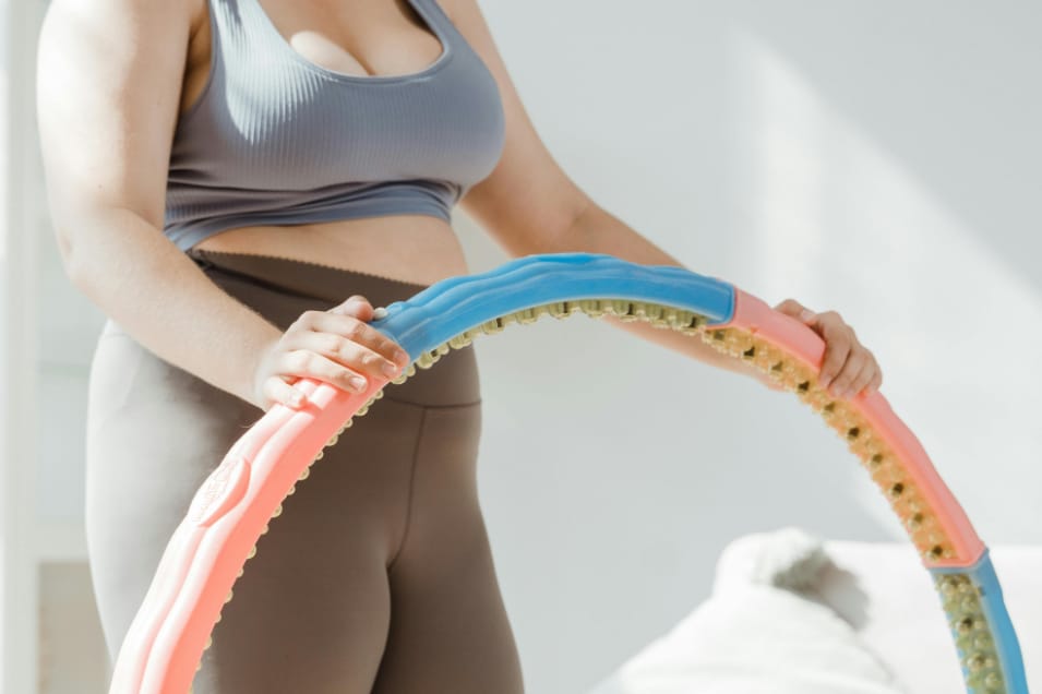Woman in blue sports bra and brown leggings holding a hula hoop.